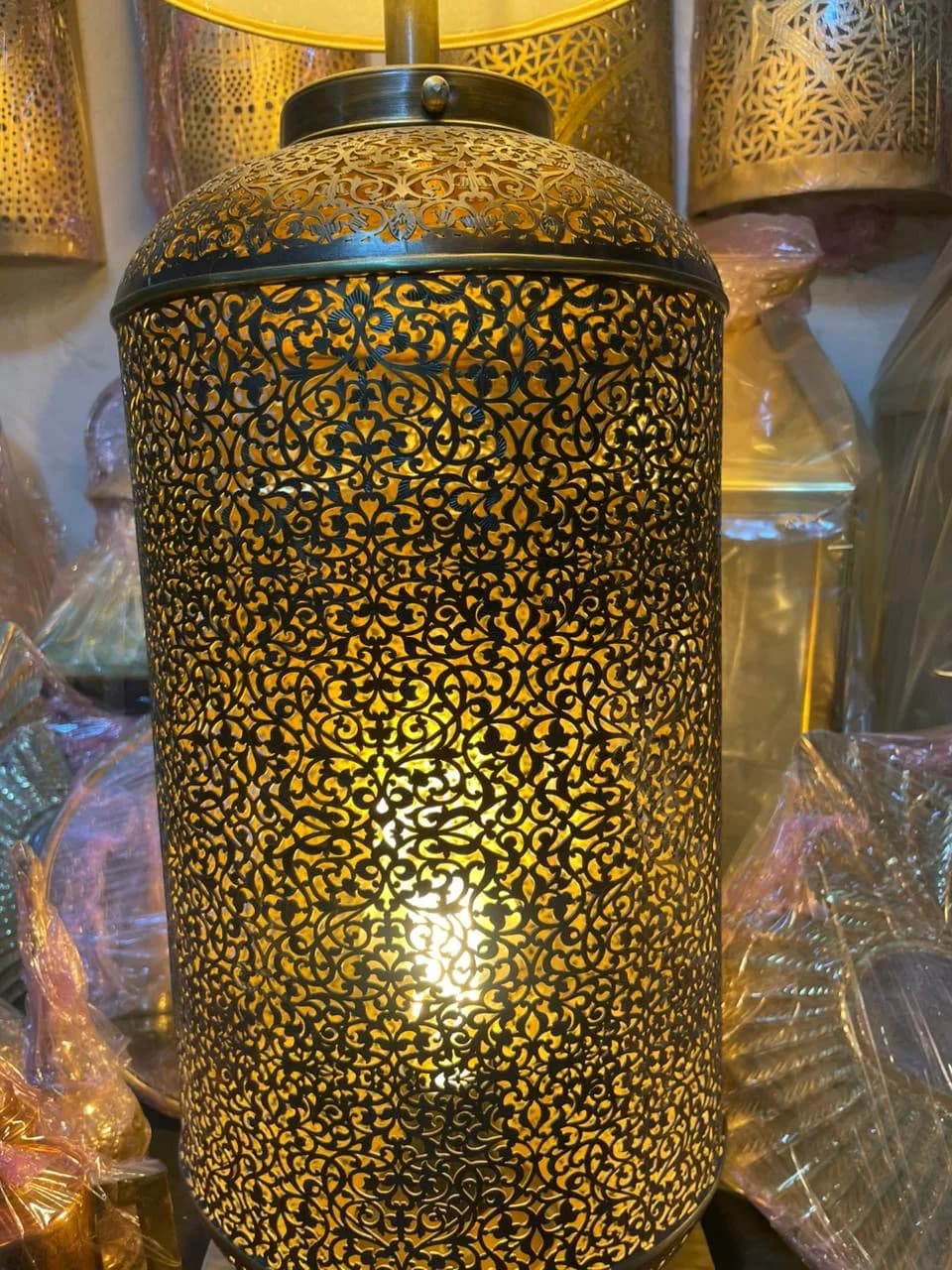Close view of a pierced brass lamp body, lit from inside so the arabesque cut-work glows