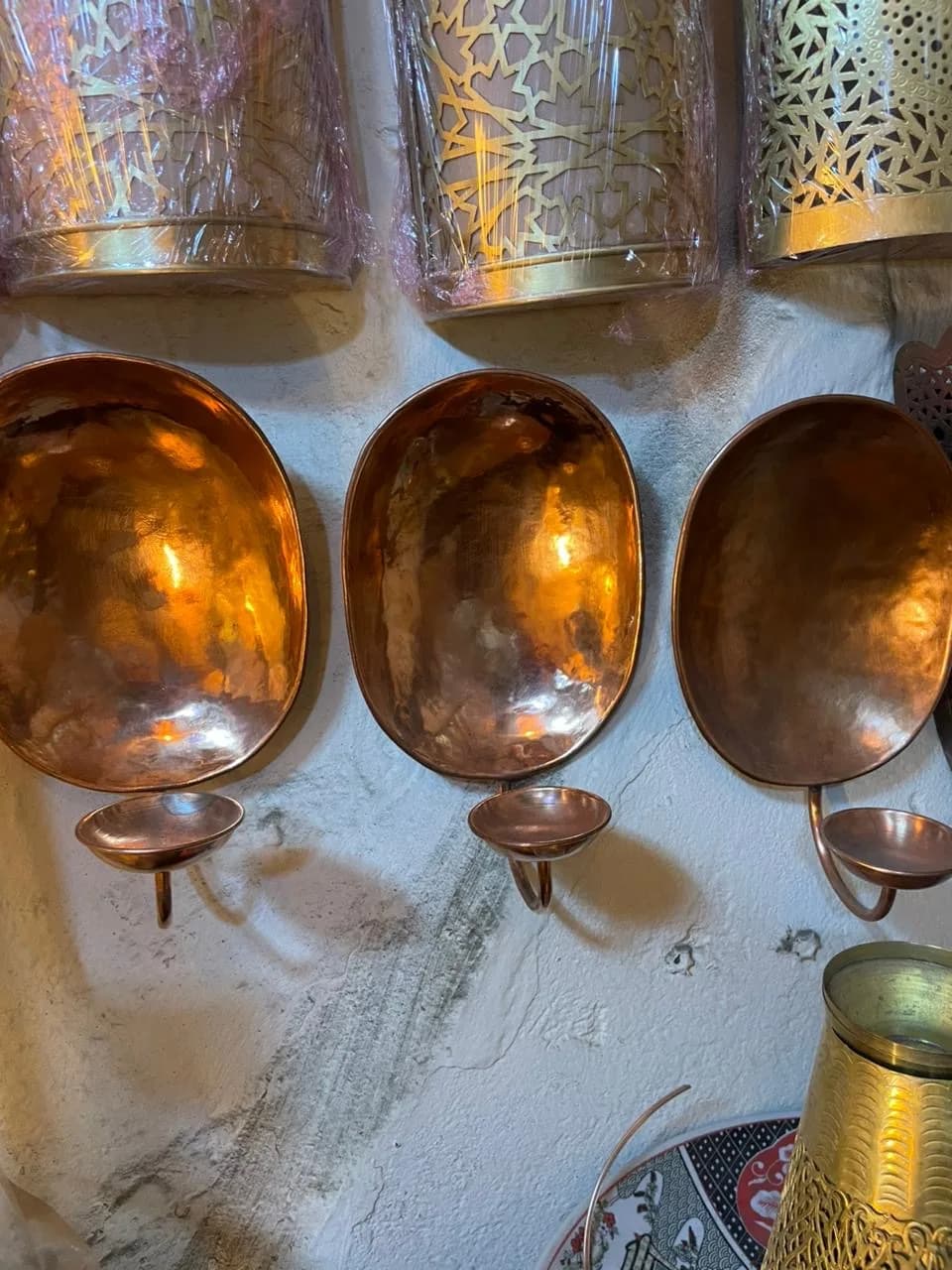 A hand-hammered copper wall sconce with a small candle dish, mounted on a lime-plastered wall
