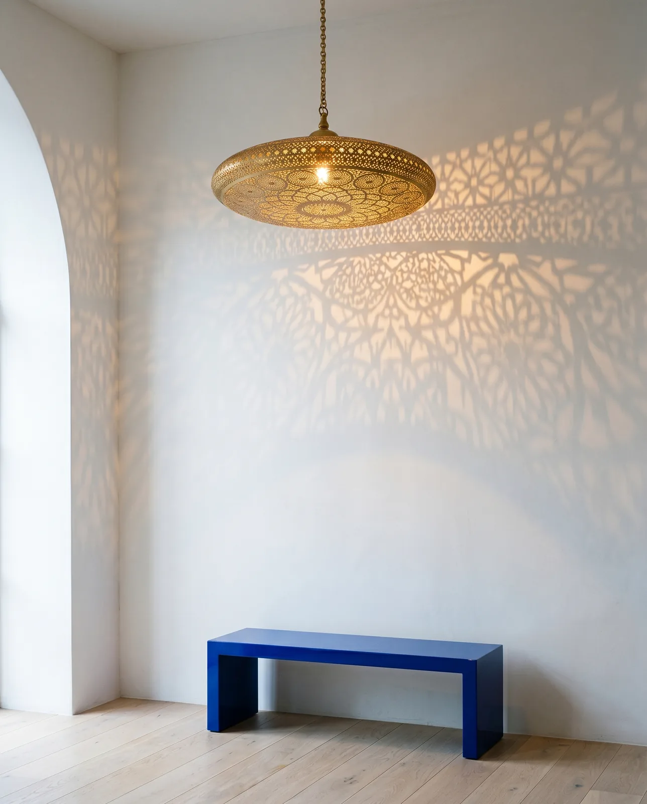 Alhambra hand-pierced brass pendant casting a mandala shadow on white plaster